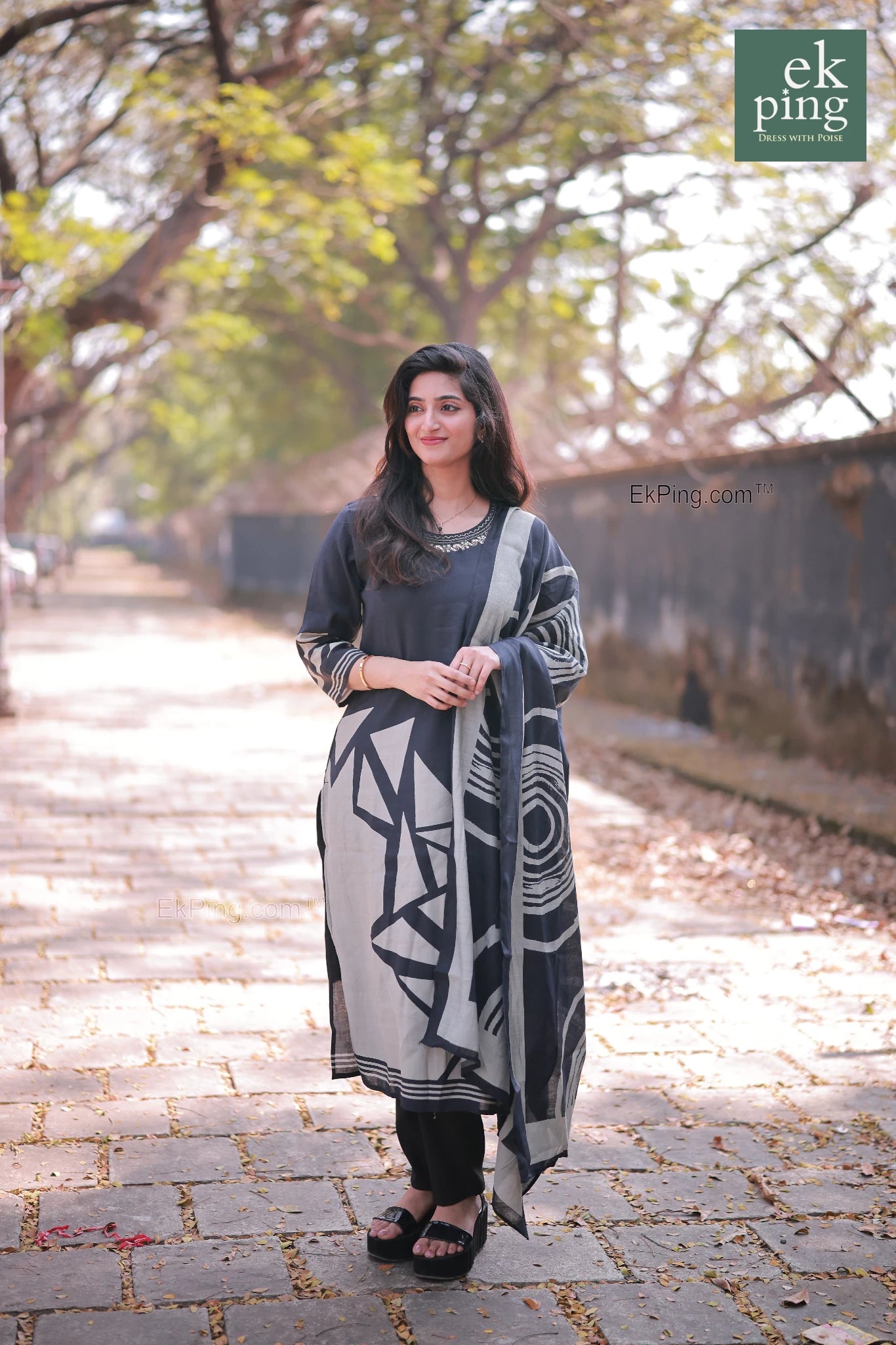 Woman wearing a black daily wear long kurti and salwar set standing on a paved path with trees in the background