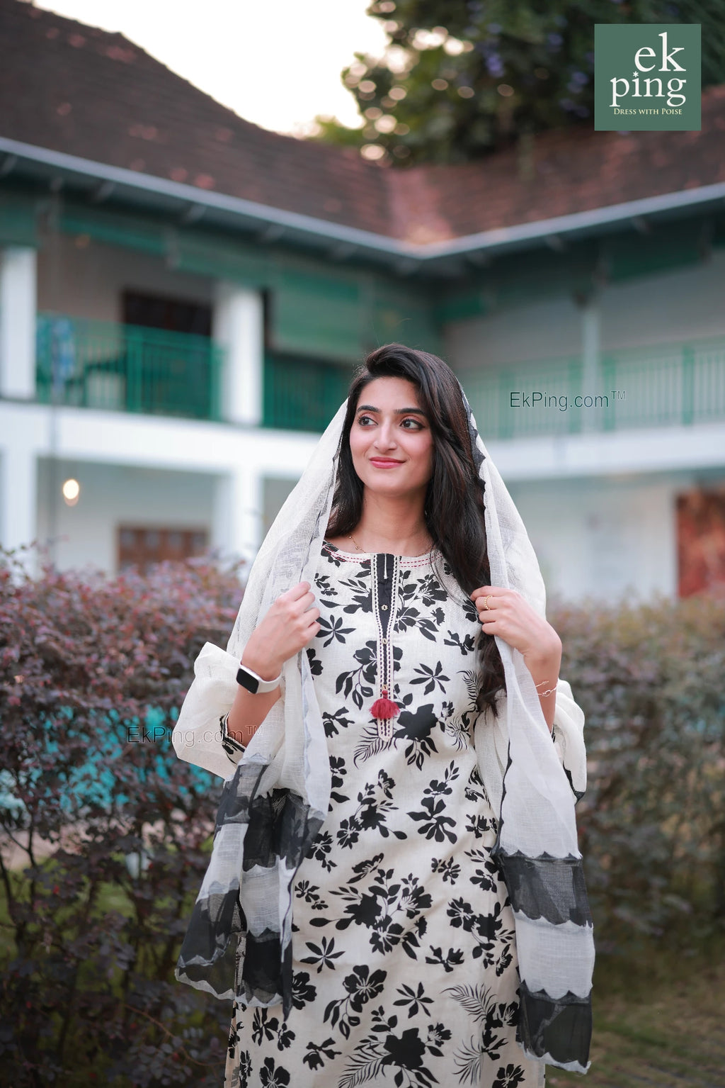 Woman in a floral white and black floral Salwar dress with a white dupatta standing in front of a building.