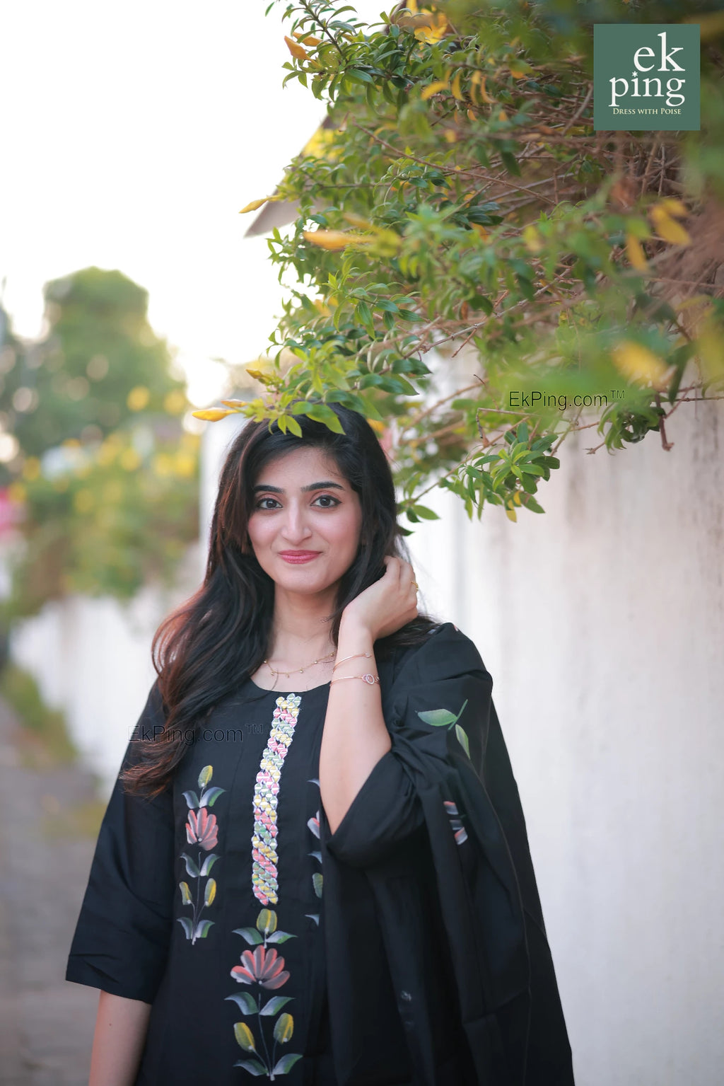 Woman wearing a black salwar set standing outdoors with greenery