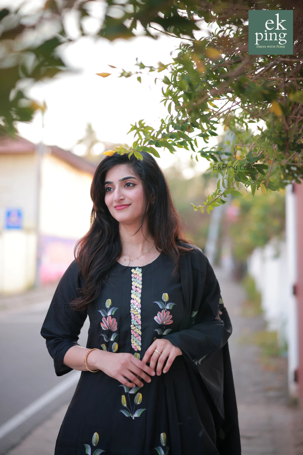 Woman in a black salat set dress standing outdoors with greenery in the background