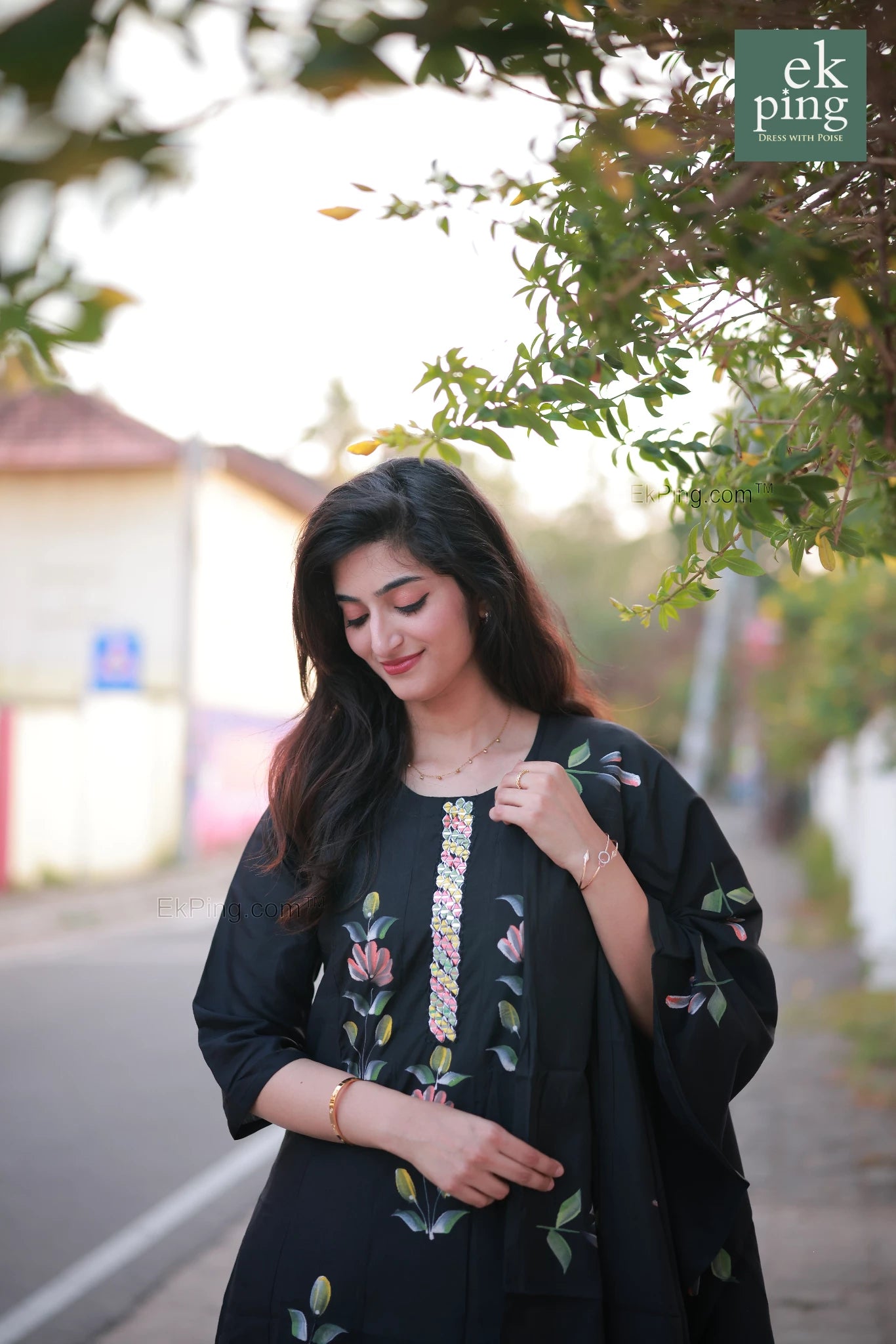 Woman wearing a black salwar outfit standing outdoors with greenery in the background