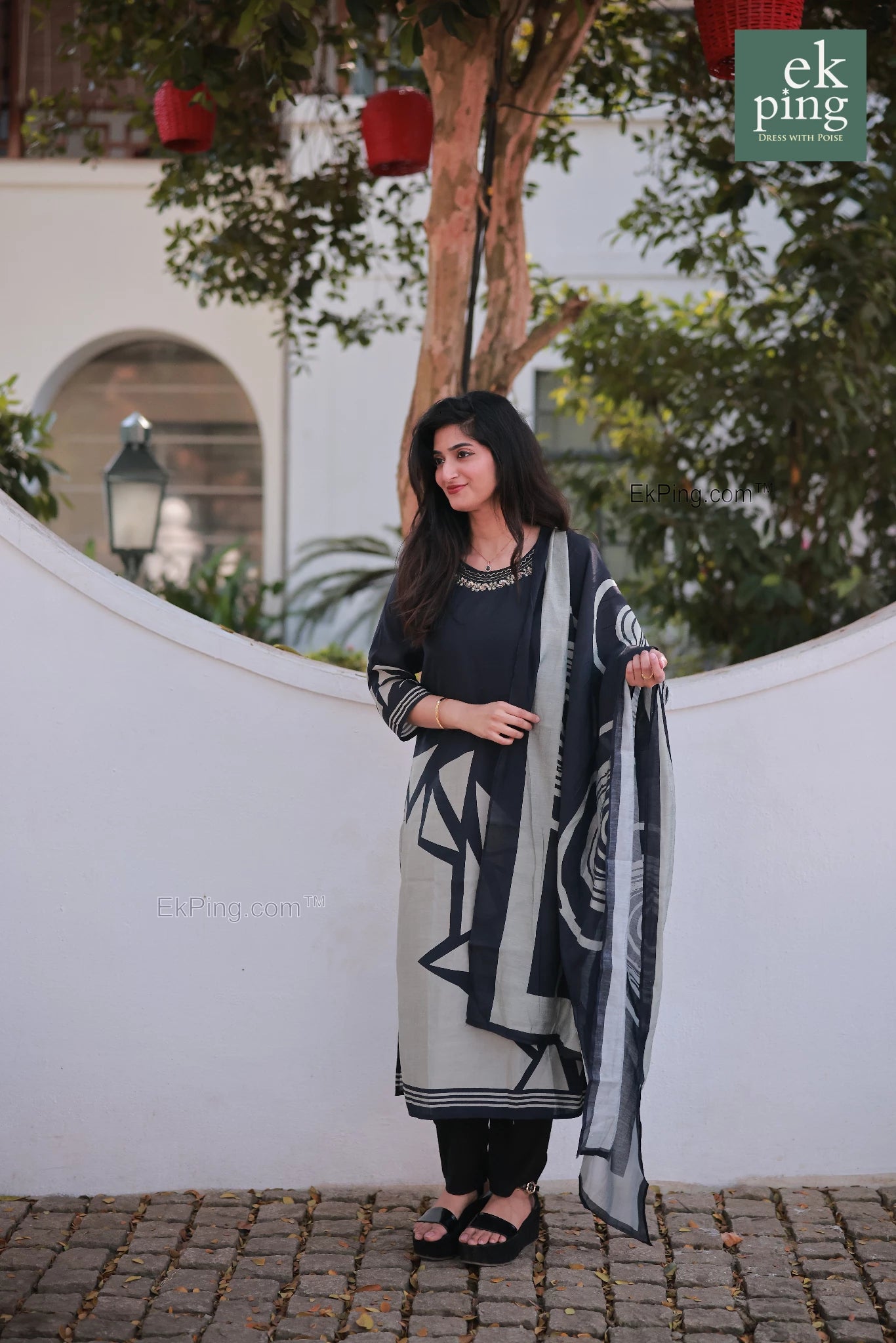 Woman holding a black and white patterned salwar kurti outdoors with greenery in the background