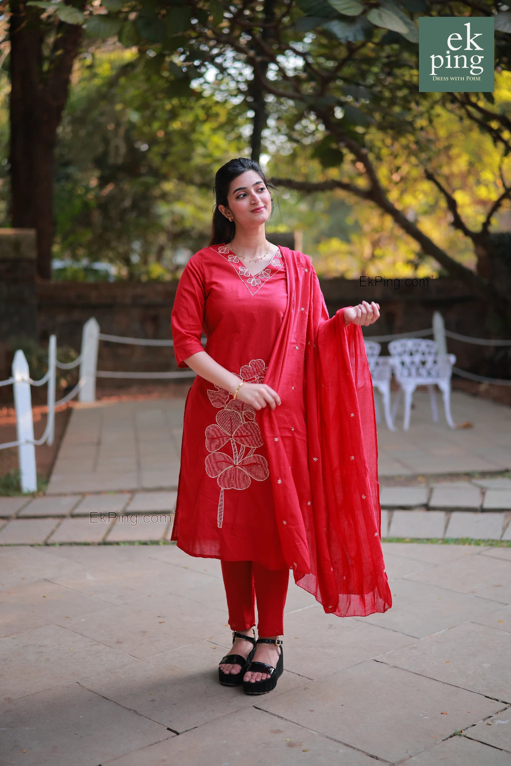 Woman in a red salwar with cigerette pants standing outdoors with greenery in the background