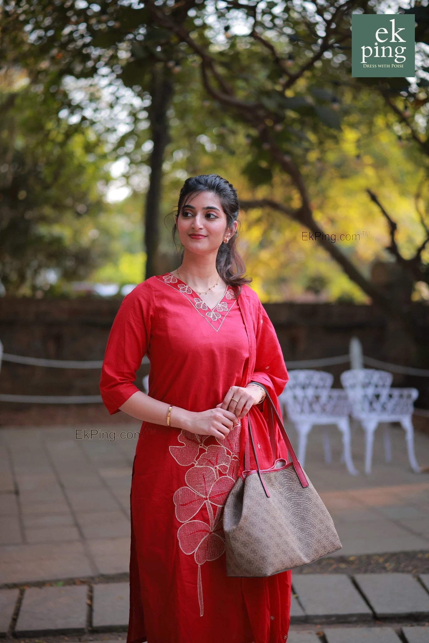 Woman in a red salwar with cigerette pants standing outdoors with chairsin the background