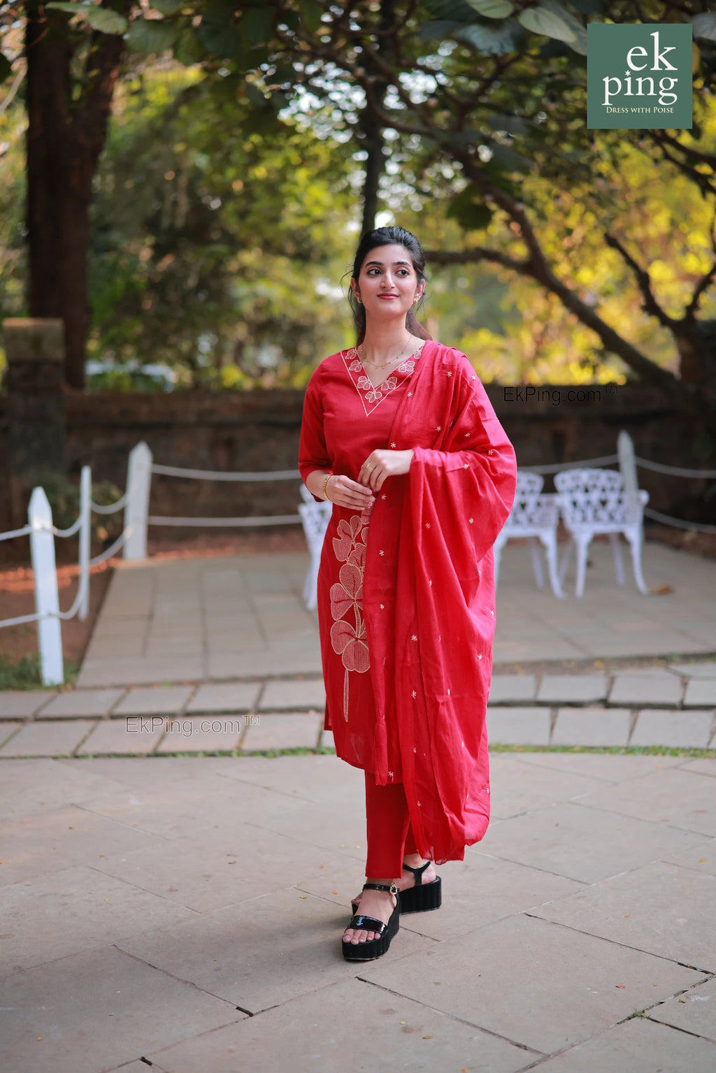 Woman in a red kurti standing outdoors with greenery in the background