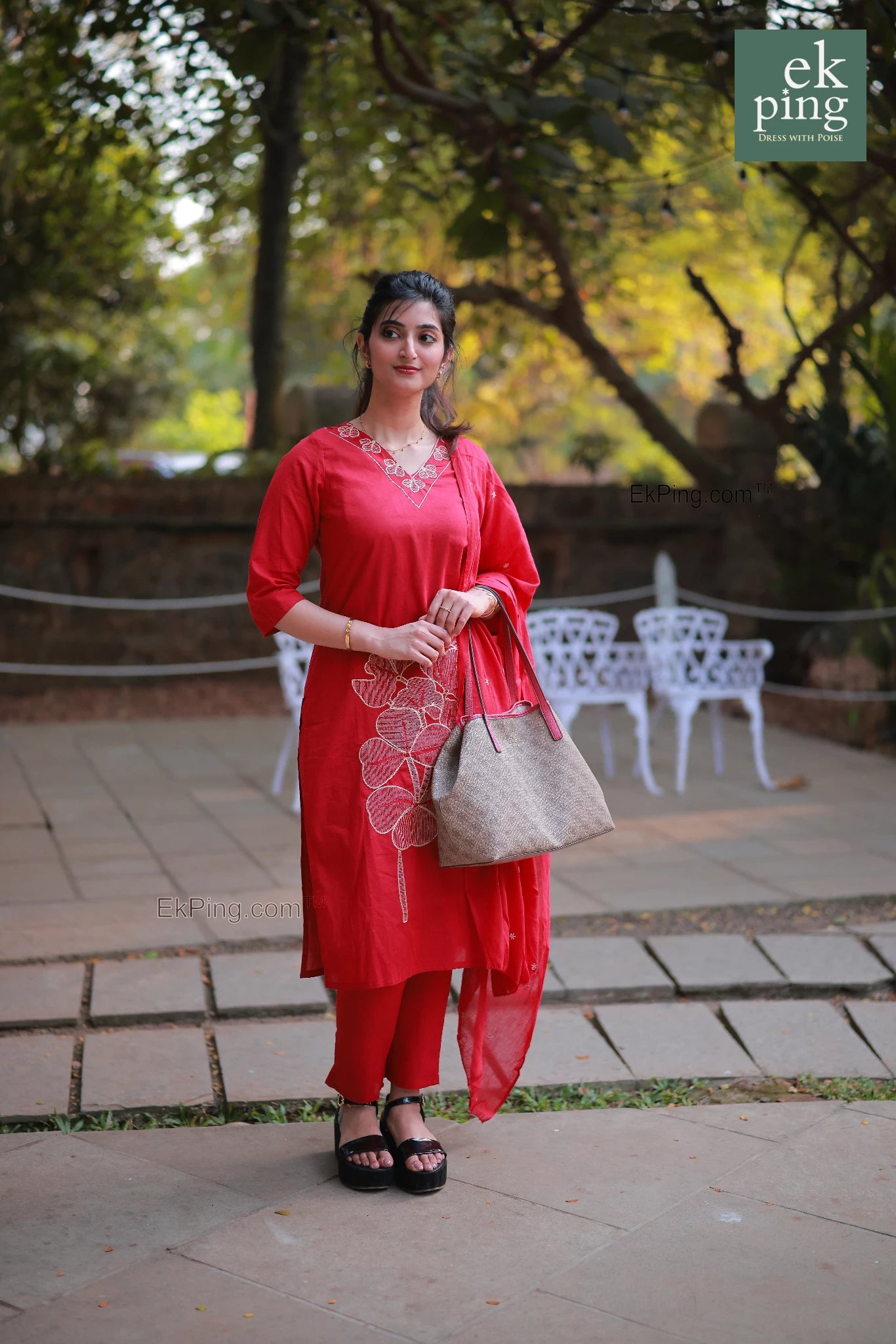 Woman in a red kurti standing outdoors with greenery in the background