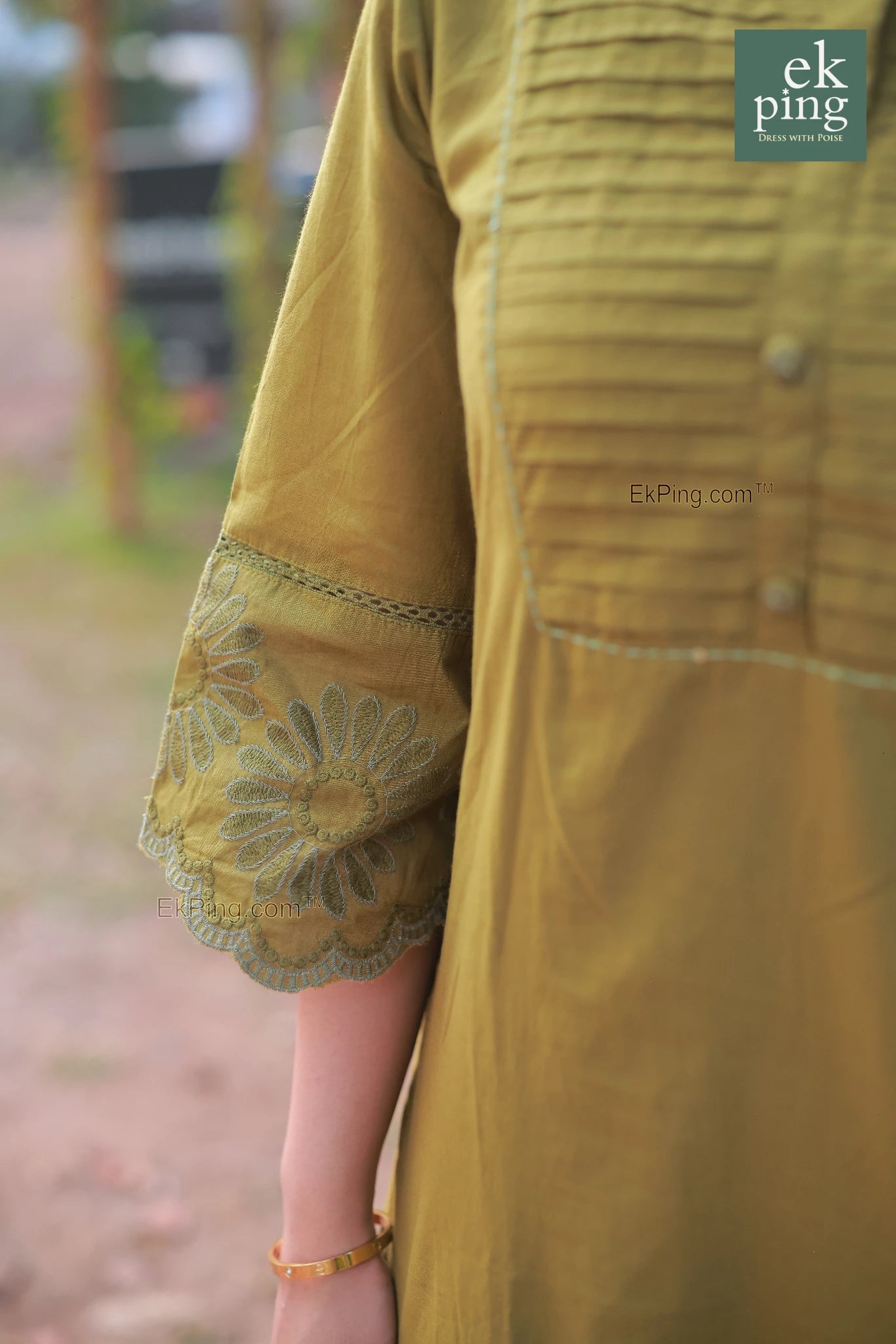 Close-up of a green co-ord set with floral embroidery on a blurred outdoor background