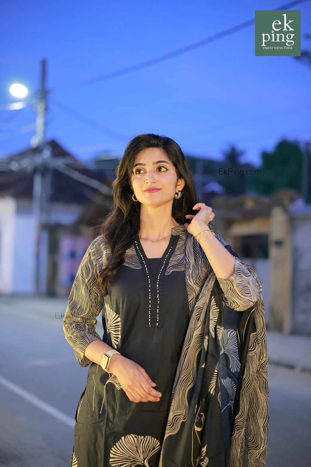Woman in a navy black salwar kurti with a patterned shawl standing on a street at night.