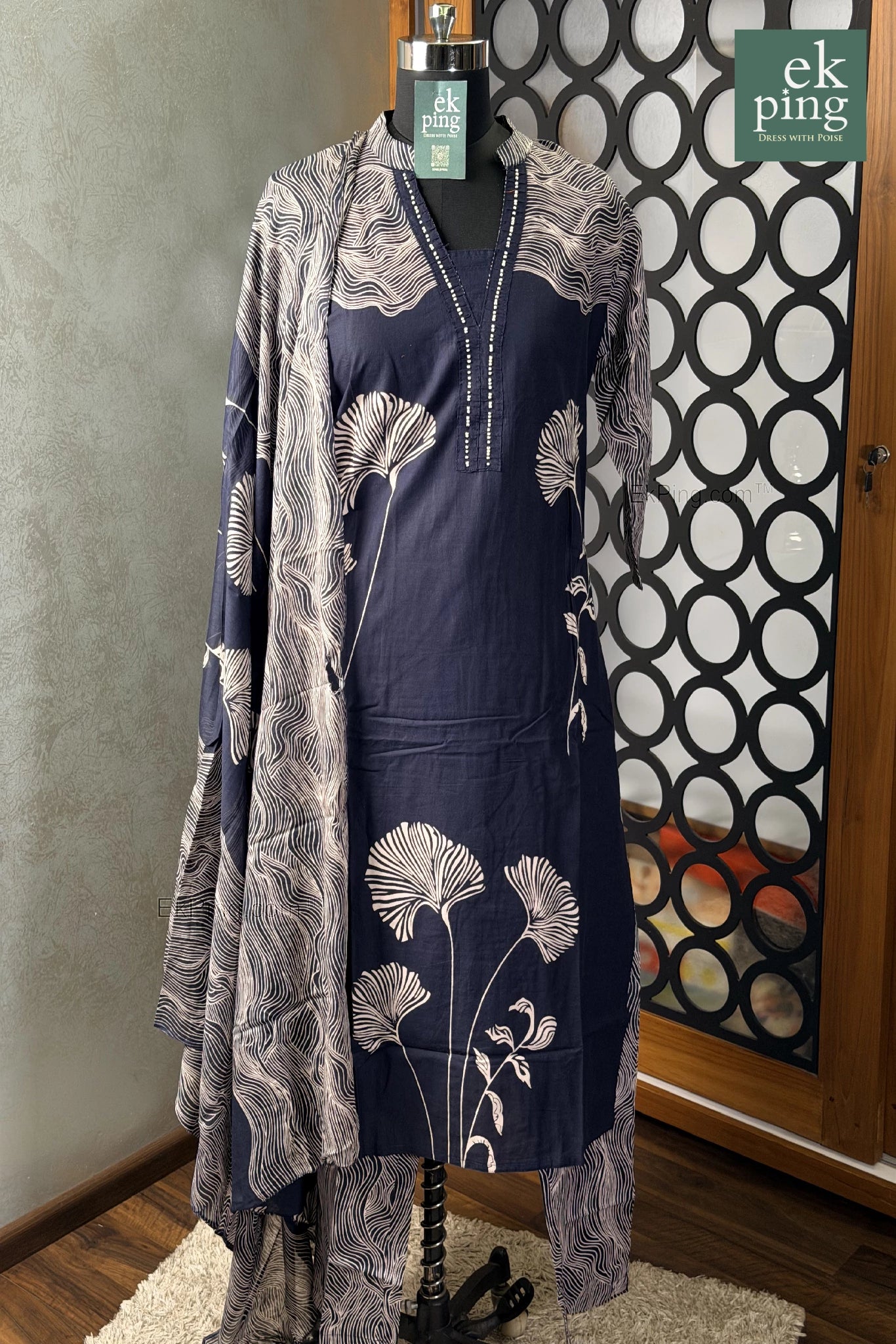 Navy dress with floral pattern and matching shawl on a manequin against a decorative wall.