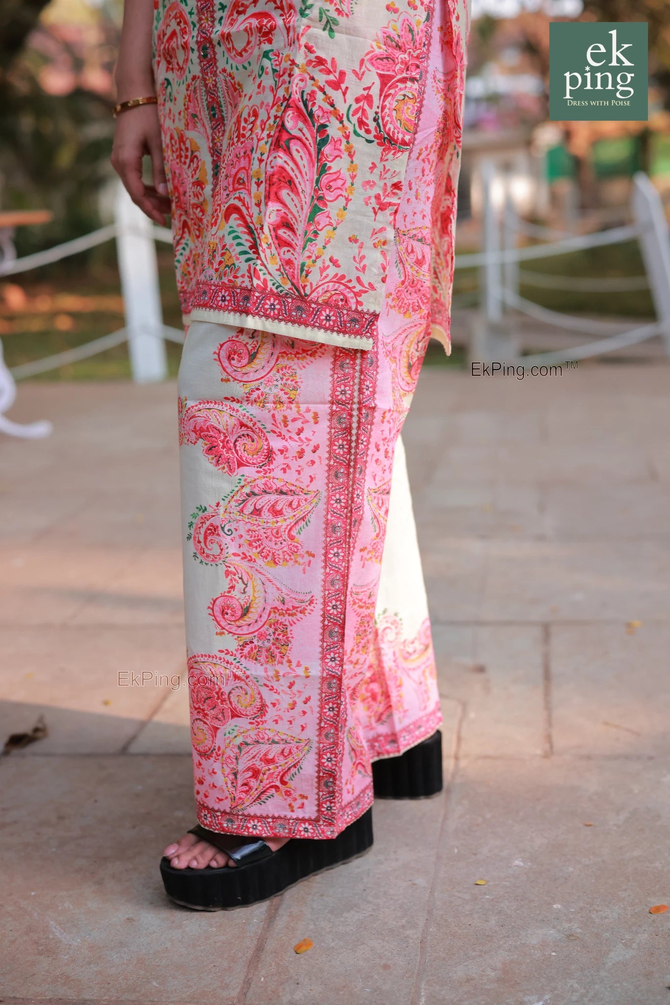 Woman in a pink floral co-ord set with palazzo pants with black shoes on a blurred outdoor background.