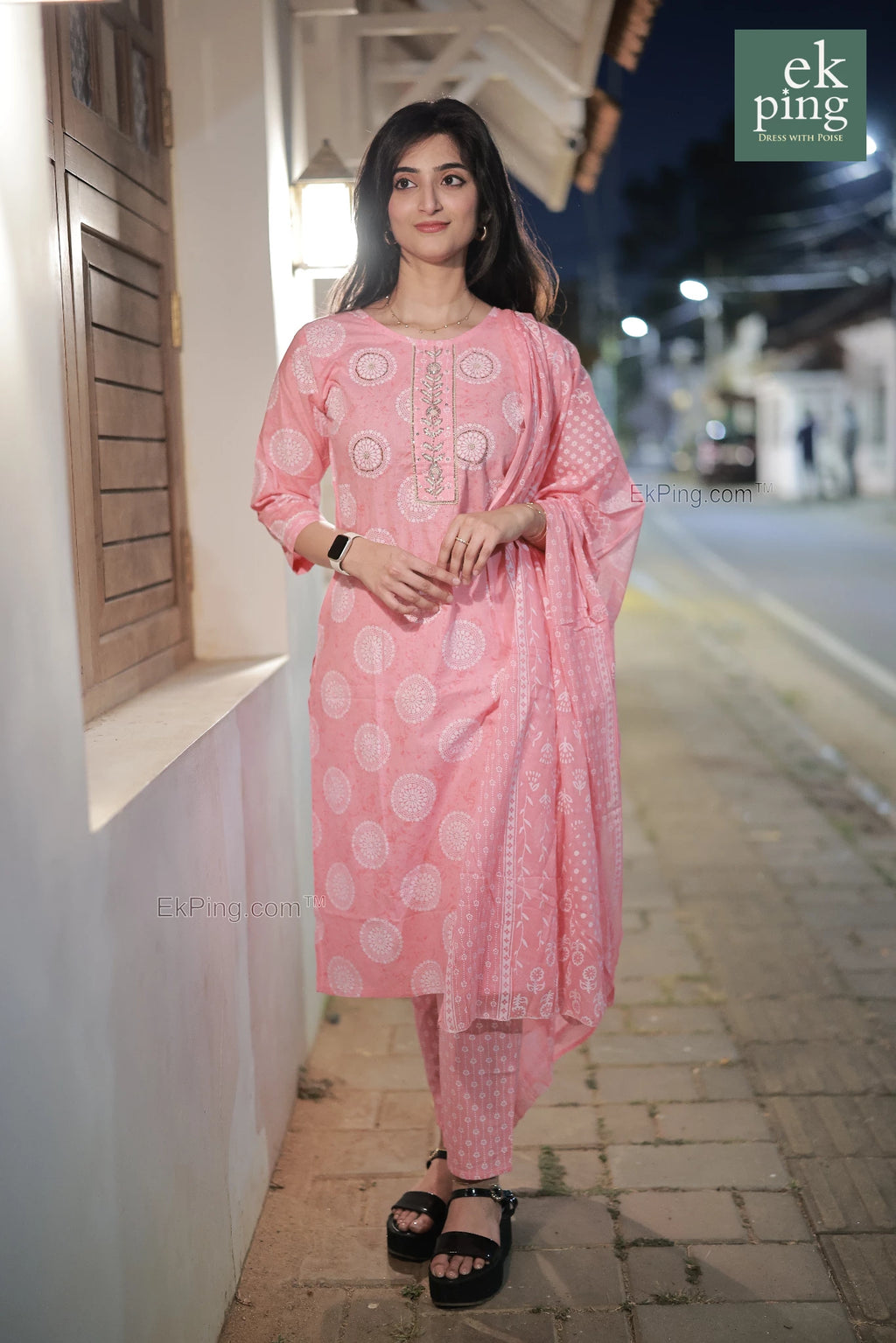 Woman in a pink cotton salwar set standing on a street at night