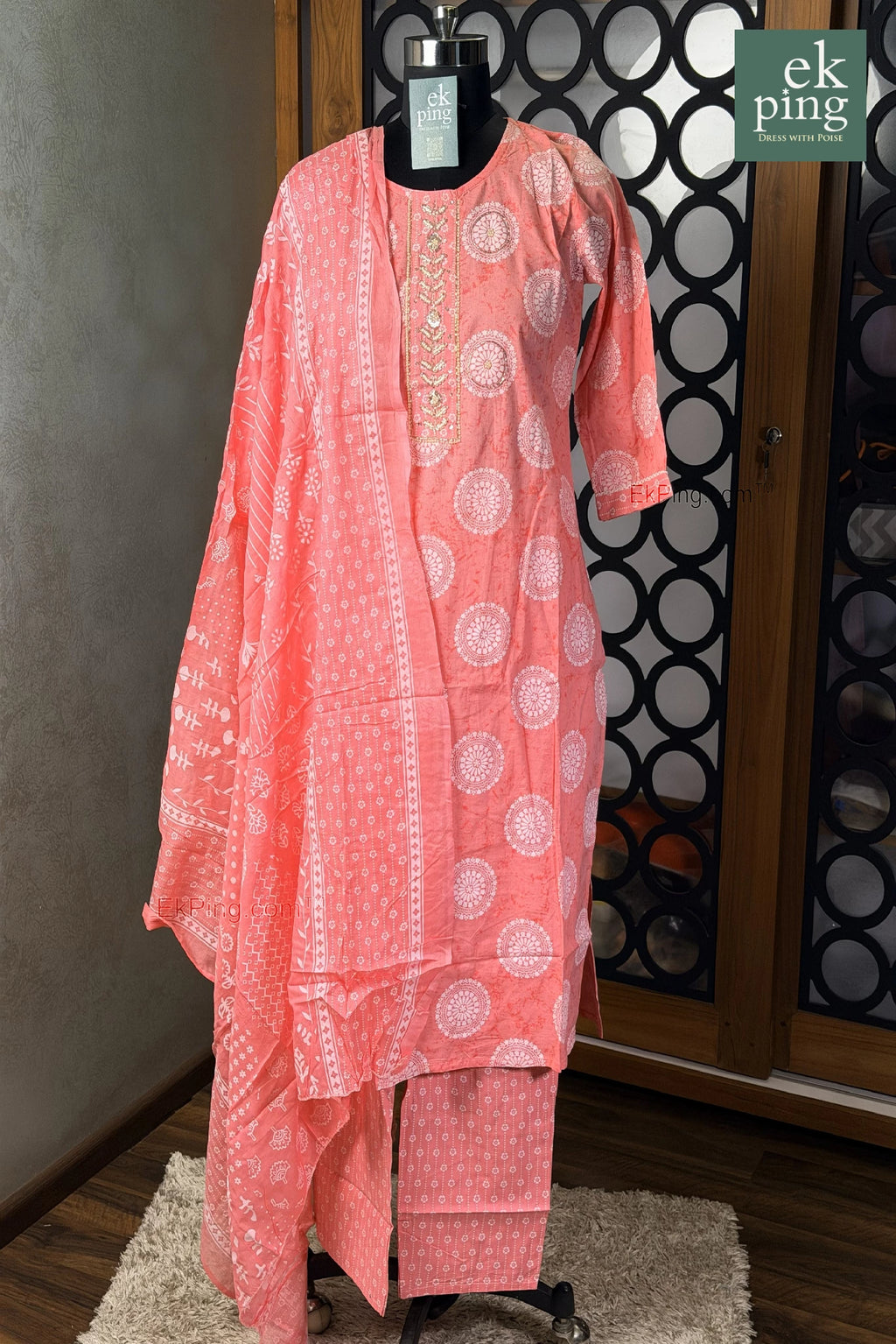 pink cotton salwar set with white patterns on a mannequin against a decorative wall.