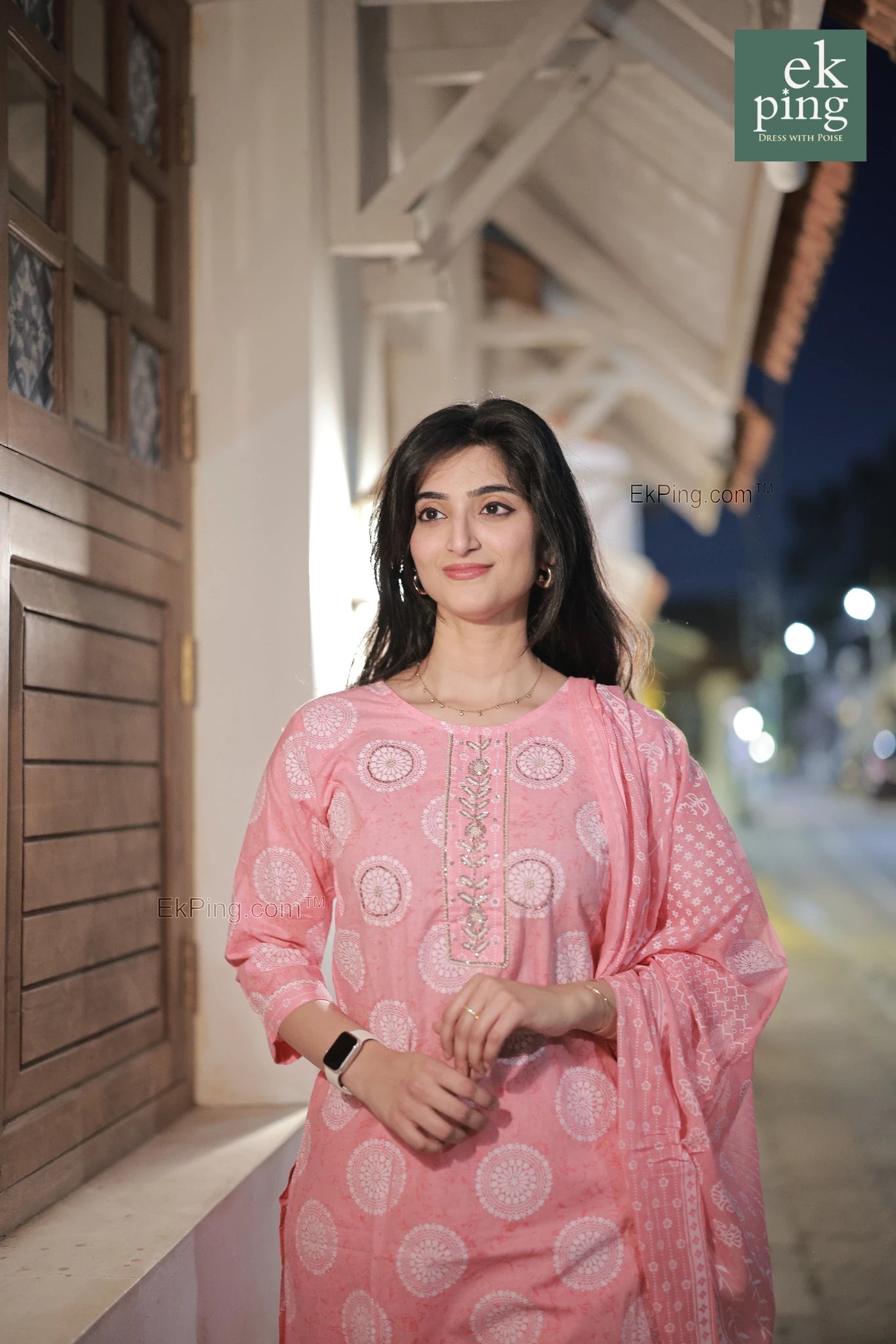 Woman in a pink cotton salwar set standing outdoors at night.