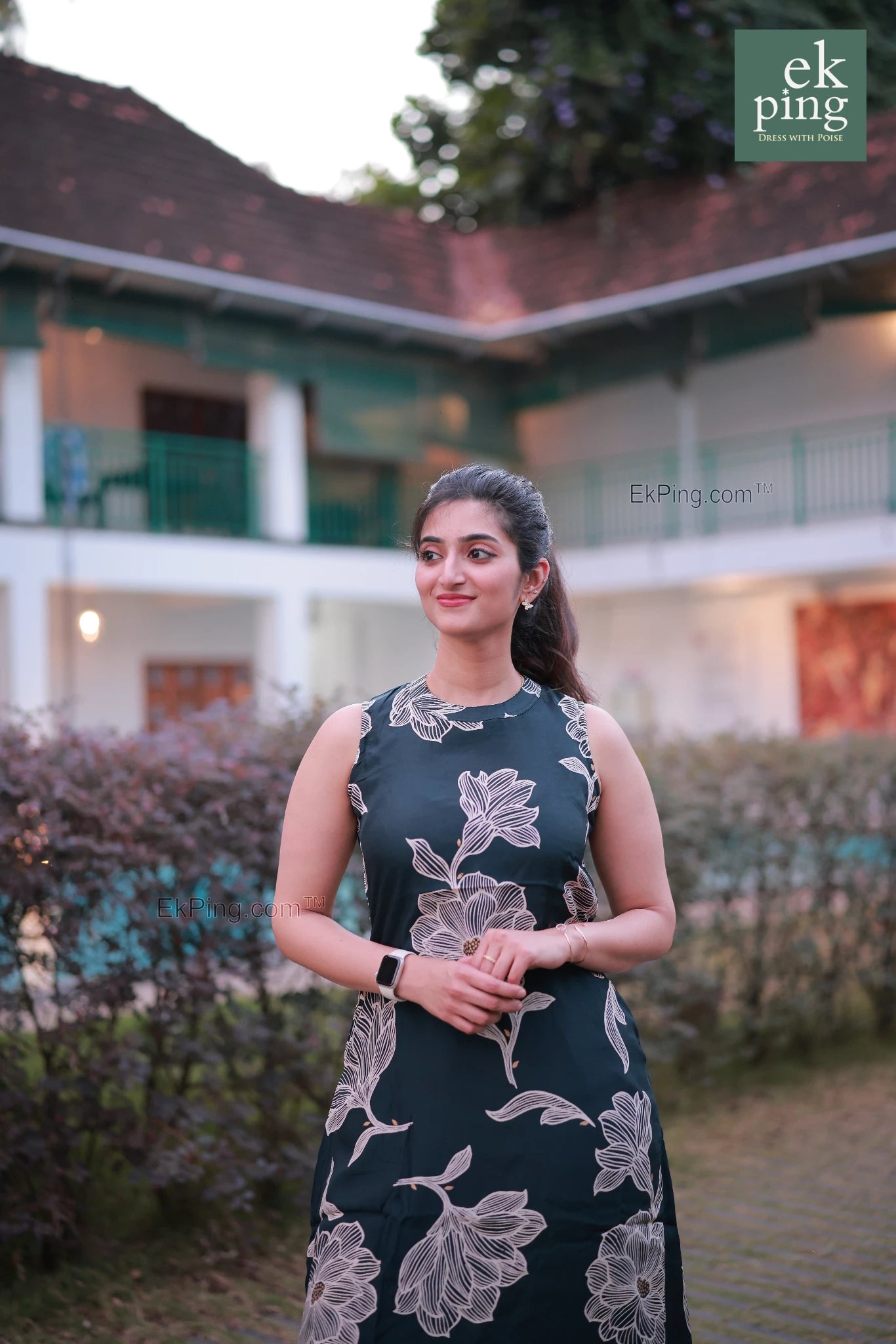 Woman in a sleeveless office wear standing in an outdoor setting with plants and resort in background