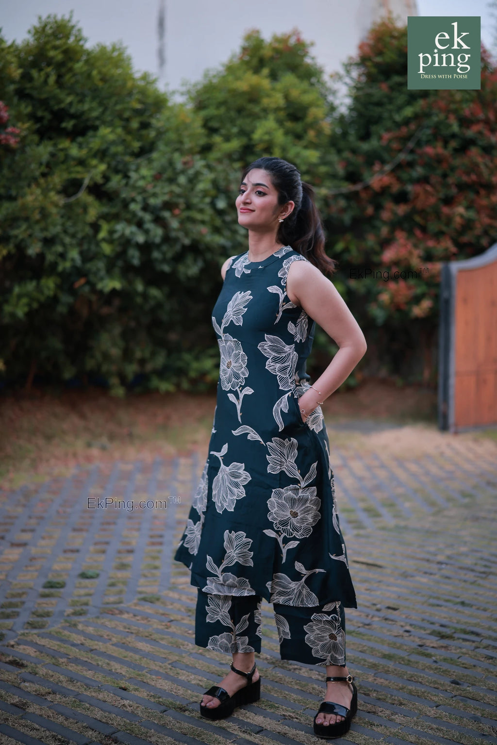 Woman wearing a sleeveless office wear standing outdoors with greenery in the background