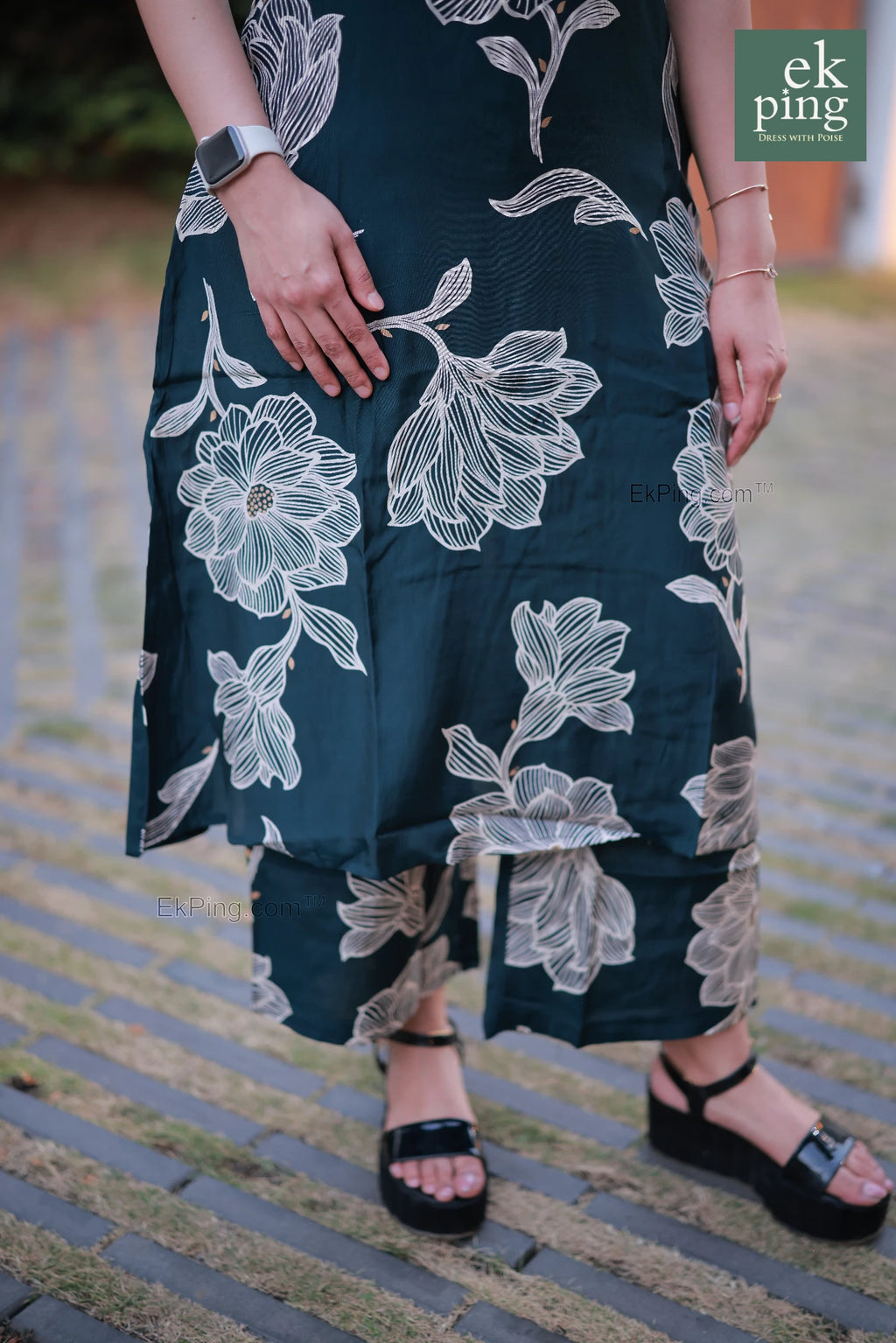 Woman wearing a sleeveless office wear with white floral patterns on a blurred outdoor background.