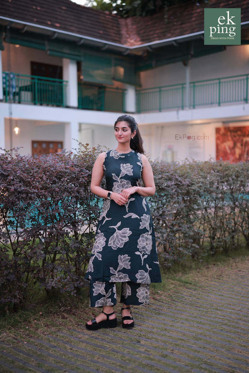 Woman in a sleeveless office wear standing outdoors with greenery and a building in the background