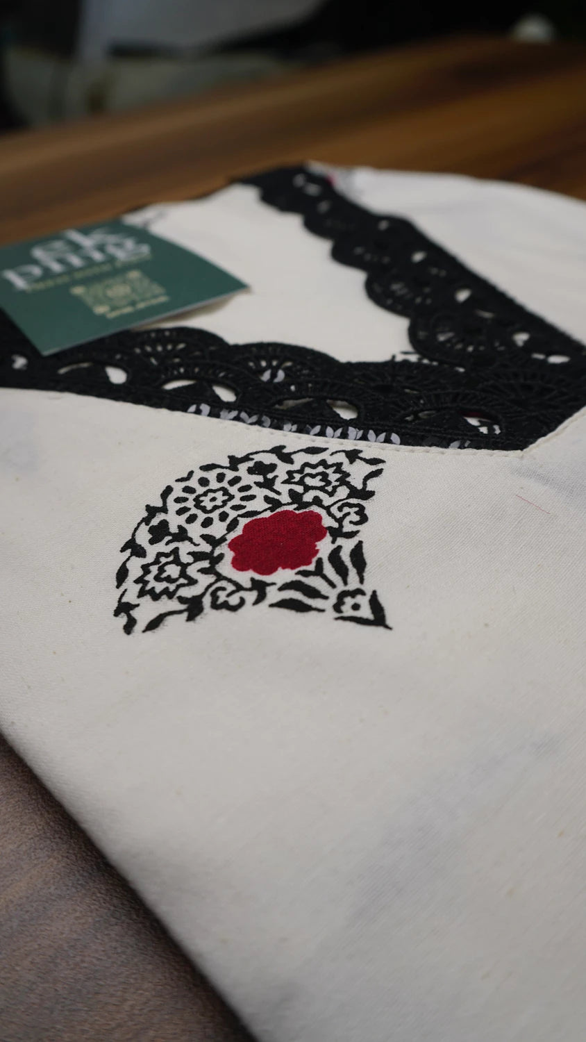 Close-up of a white kurti top with black lace and red flower design, on a table