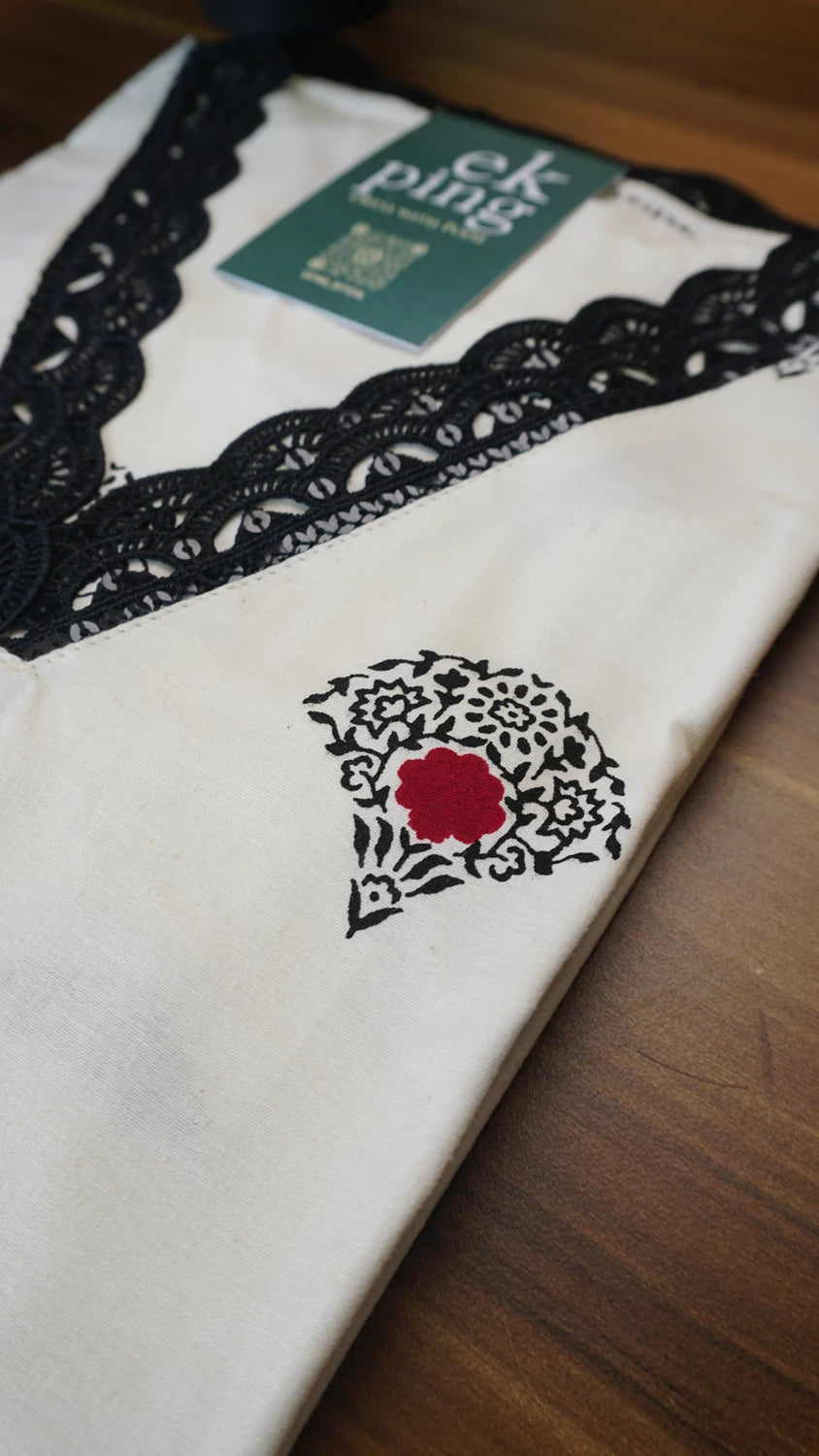 White garment with black lace trim and red rose design on a wooden surface
